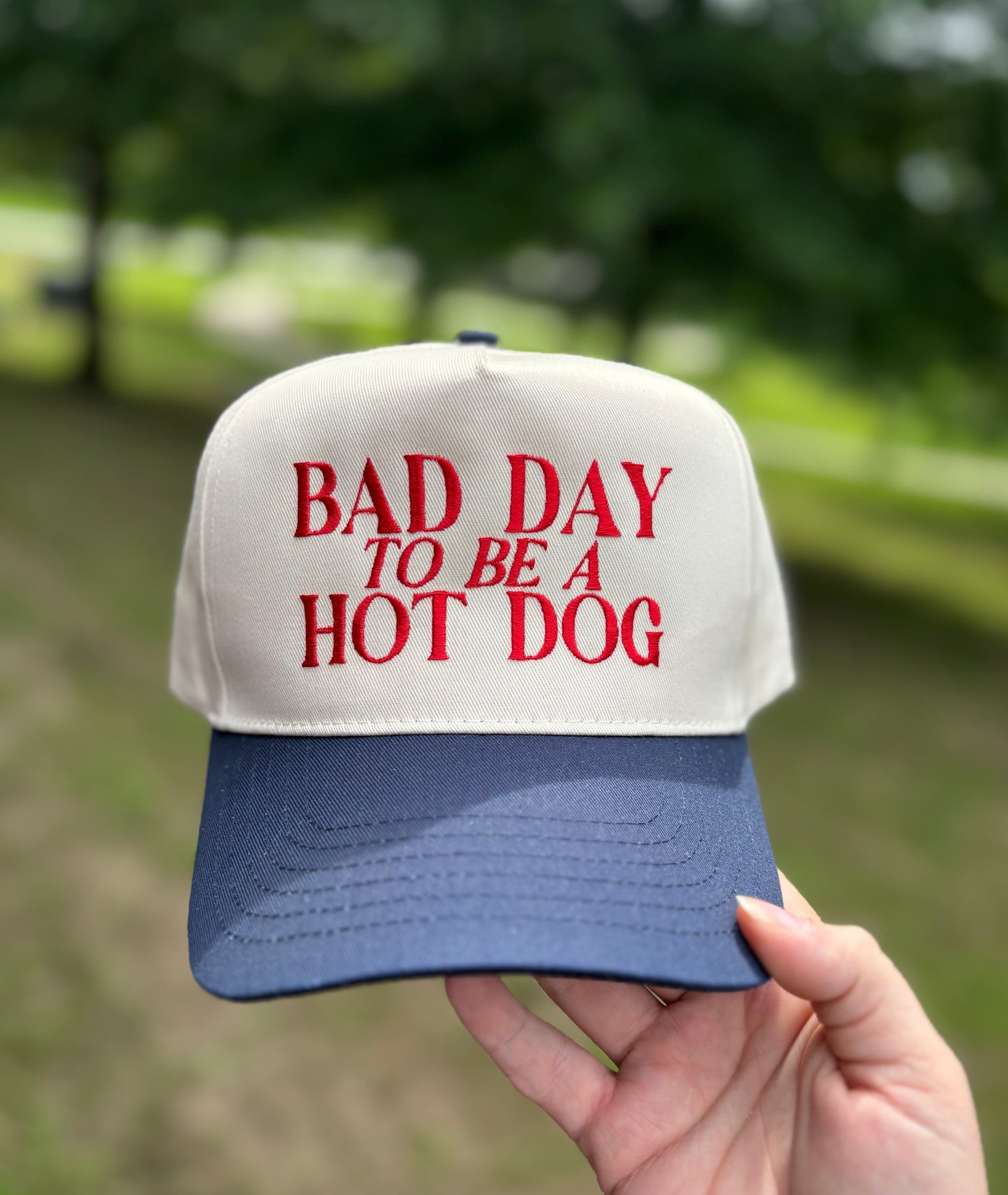 Cap with 'Bad Day to be a Hot Dog' text held in front of a blurred natural background