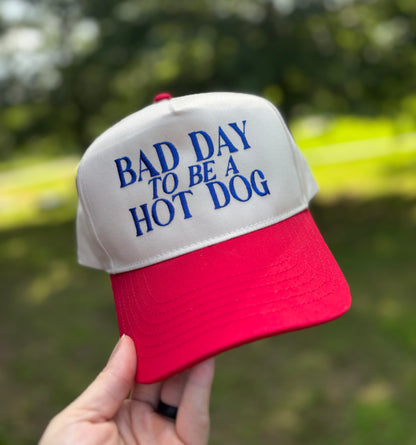 Cap with 'Bad Day to be a Hot Dog' text held in front of a blurred green background